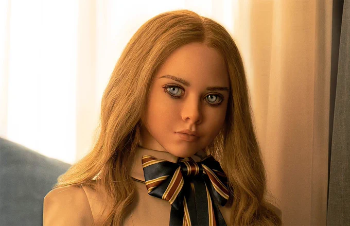 M3GAN the animatronic doll. She has pale blue eyes, blonde hair, and pale skin. She is looking menacingly just off camera.