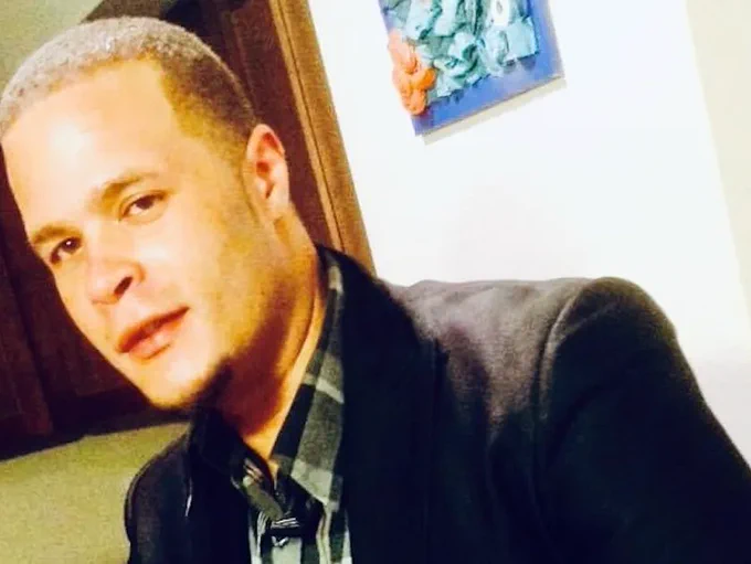 Anthony Mitchell Jr. smiles in a black jacket and dark plaid button up shirt