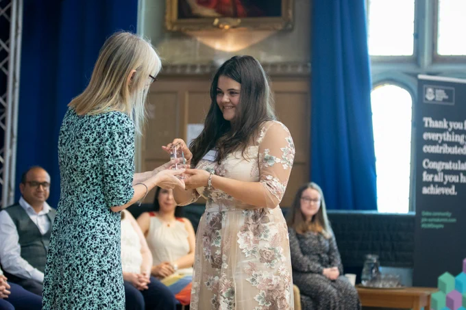 A student accepts a trophy plaque from the Dean of Sheffield University Management School, on stage in Firth Hall