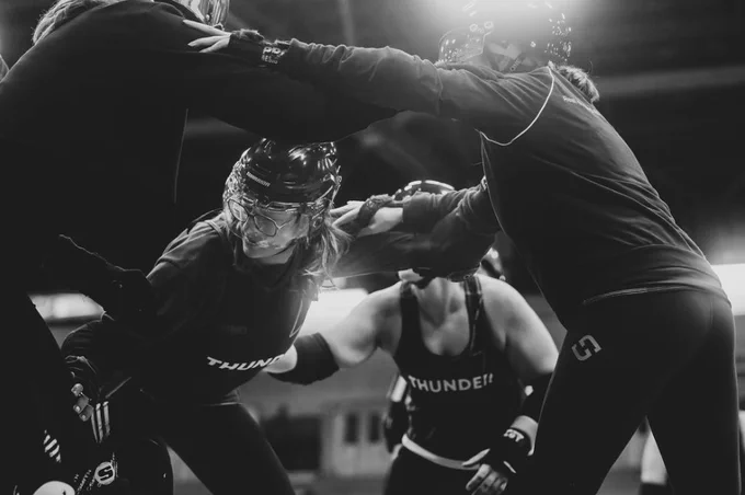 Four people wearing black jerseys playing roller derby. 