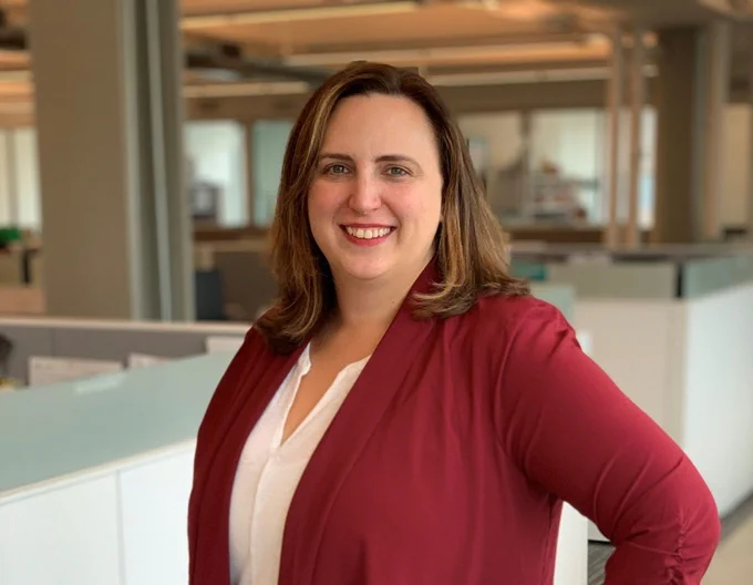 Meredith Topalanchik standing and facing the camera. She has one hand on her hip and is smiling at the camera.
