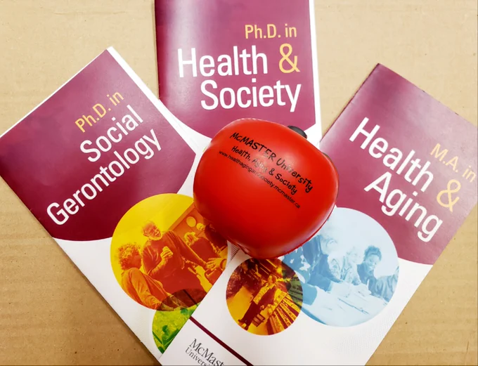 Photo of Department of Health, Aging & Society graduate program brochures with Health, Aging & Society apple-shaped stress ball.