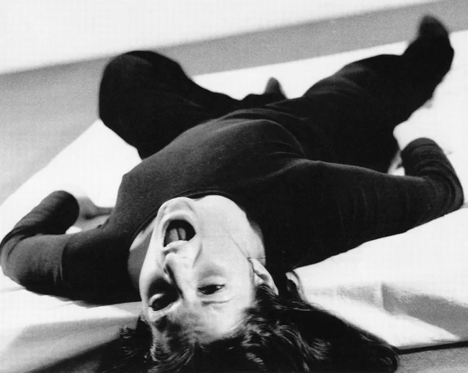 Black and white videography still of Marina Abramović laying on her back screaming in an attempt to lose her voice.
