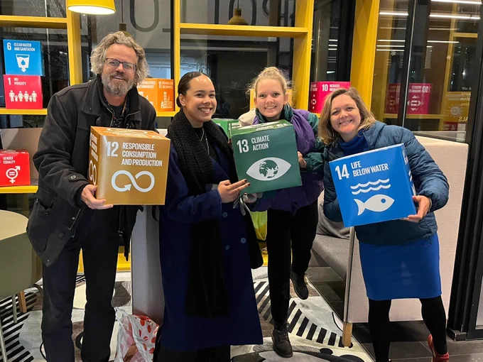 Four team members of Feedback EU/Global with three boxes in their hand that represent three Sustainable Development Goals (12: Responsible Consumption & Production; 13: Climate Action; 14: Life Below Water.)