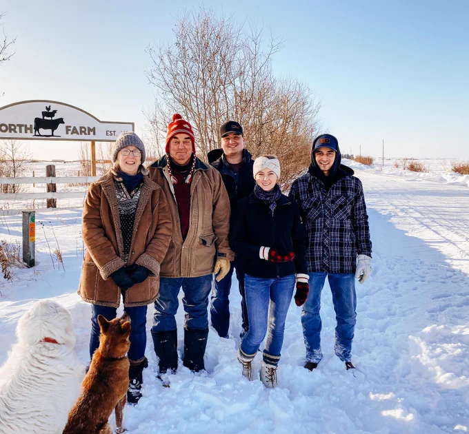 A family photo of two women and three men and two dogs in a winter scene. 