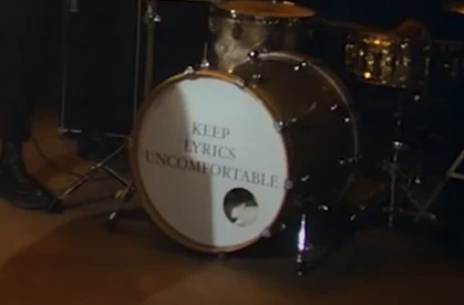 Photograph of a drum with the words, "Keep lyrics uncomfortable" written on the skin.