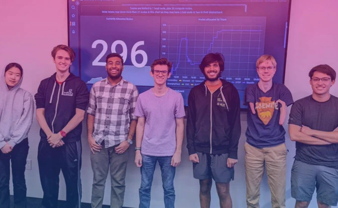 Seven students stand in front of a television screen that displays their work from the IndySCC competition. 