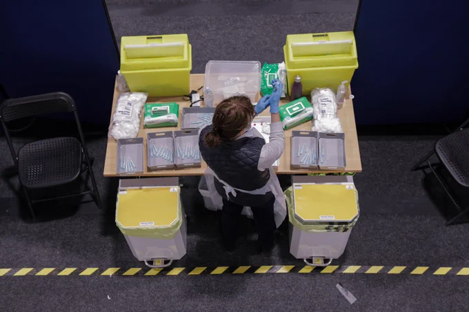 an overhead photo of a nurse filling syringes with meds at a desk with sharp boxes and bins next to her