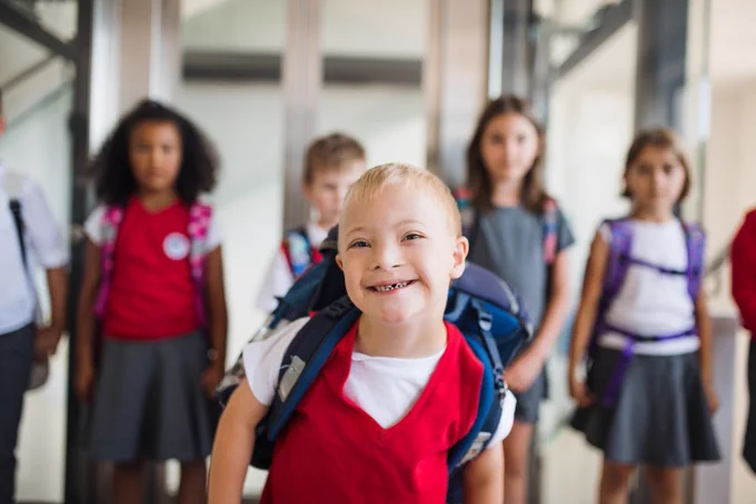 A child in a red tank top at school with other children walking behind.