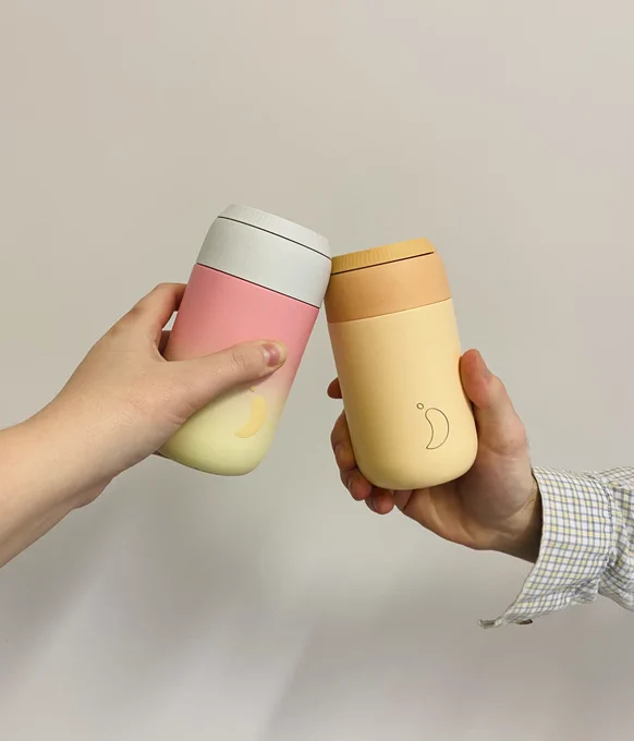 Two hands holding reusable coffee cups and doing a little ‘cheers’
