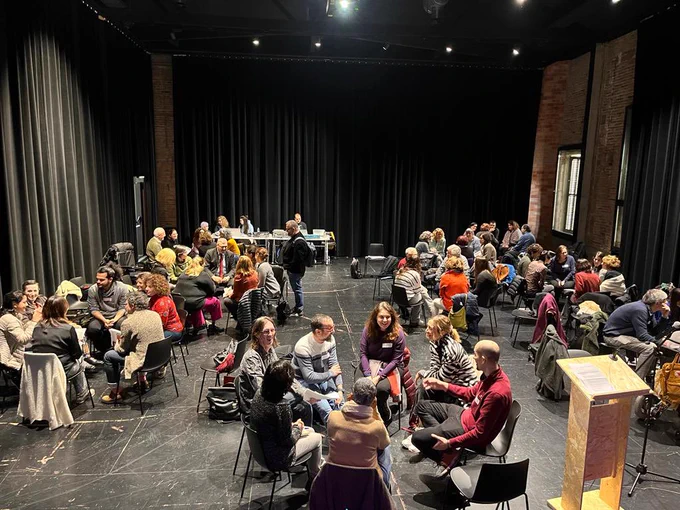 Una sala grande con muchas personas sentadas en grupos haciendo dinámicas