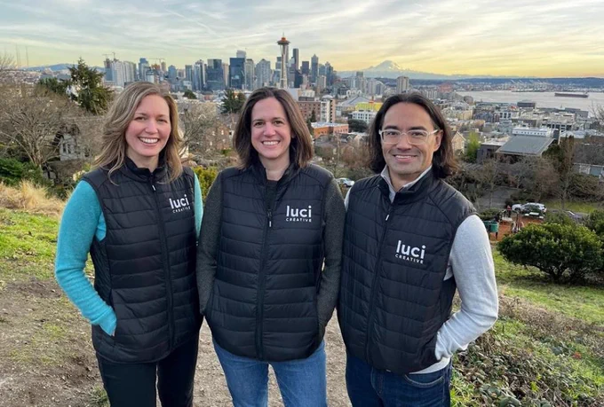 Three team members wearing Luci Creative jackets in front of a city background