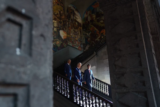 Prime Minister Justin Trudeau, President Andrés Manuel López Obrador, and President Joe Biden are walking down a staircase. On the wall behind them, a painted mural is visible.