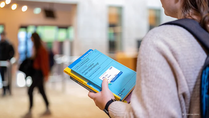 Fotoaufnahme einer Person, die mehrere Bücher in den Händen hält. Auf dem obersten Buch befindet sich zudem noch die Campuscard der TU Dresden.