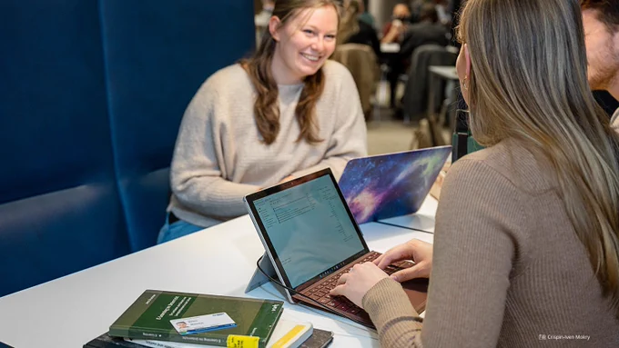 Fotoaufnahme einer dreiköpfigen Gruppe von Studierenden, die gemeinsam an einem Tisch sitzen mit aufgeklappten Laptops und Büchern. Auf einem der Bücher befindet sich die Campuscard der TU Dresden.