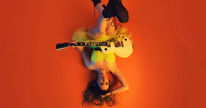 A photo showing a performer lying upside down with a guitar 