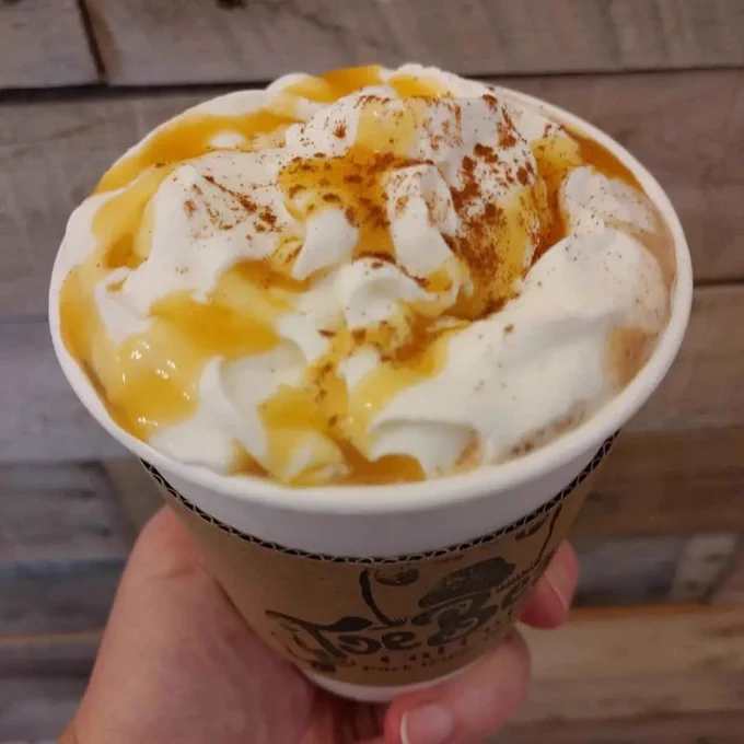 Closeup of someone holding a cup of coffee with whipped cream and caramel on top from Toe Beans Café