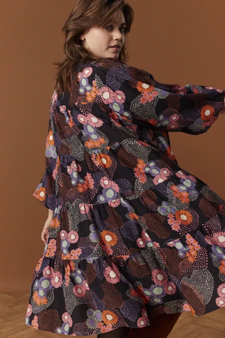 Robe ample qui tourne à 4 empiècements assemblés avec des fronces, longueur en dessous du genoux. Encolure arrondie, manches bouffantes resserrées aux poignets avec un élastique. Ouverture robe dans le dos et se referme à l'aide d'un bouton au niveau de l'encolure dos. 