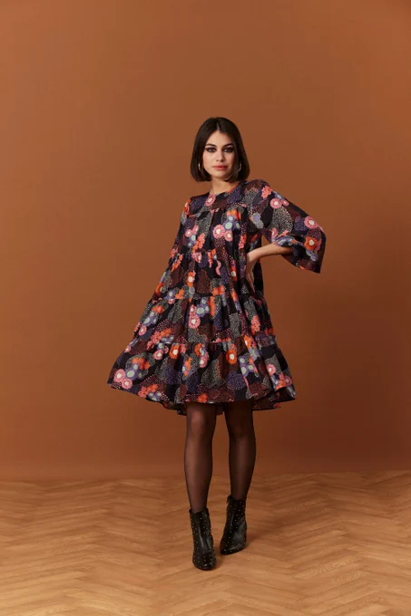 Robe ample qui tourne à 4 empiècements assemblés avec des fronces, longueur en dessous du genoux. Encolure arrondie, manches bouffantes resserrées aux poignets avec un élastique. Ouverture robe dans le dos et se referme à l'aide d'un bouton au niveau de l'encolure dos. 