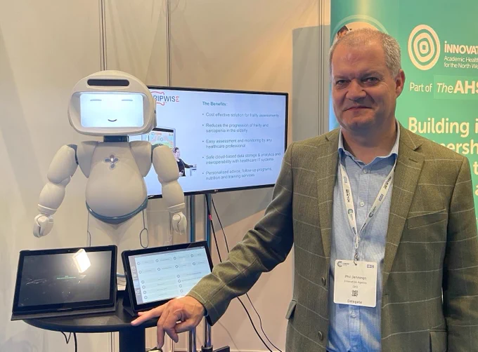 A small, smiling robot is on the left, while Innovation Agency chief executive Dr Phil Jennings is on the right