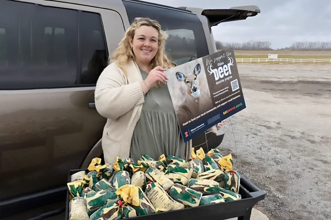 Woman holding sign in front of truck with cart full of frozen packets of donated venison.
