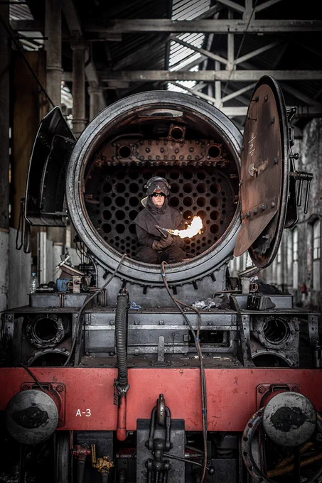 Engineer inside the nose of Flying Scotsman dressed in protective clothing with a lit blow torch.
