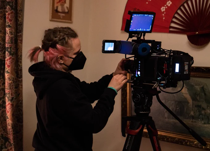 A woman wearing a face mask with pink and brown hair is adjusting a film camera