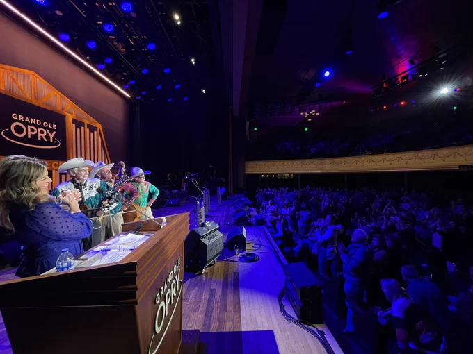 Side view of Kelly Sutton and Riders in the Sky on the Opry stage at Ryman Auditorium on the left with a standing ovation from the crowd on the right