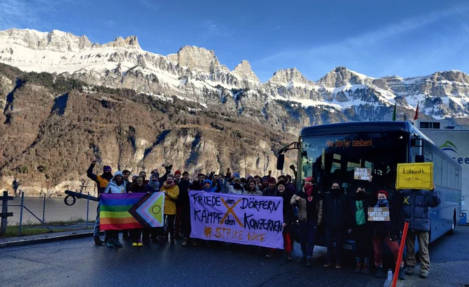 Gruppenbild mit Fahnen und Postern vorm #Solibus. Im Hintergrund schneebedeckte, hohe Bergspitzen.