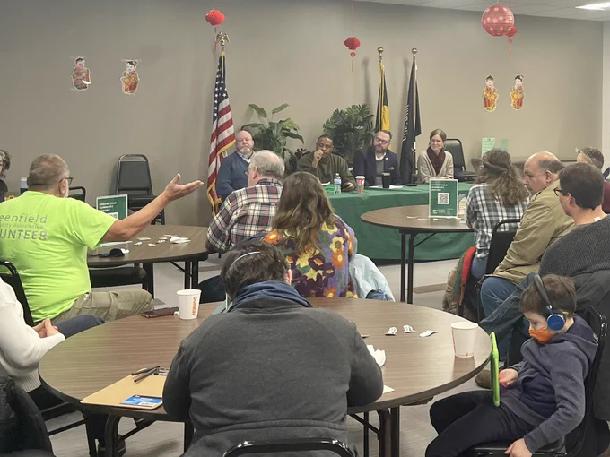 A photo of a man speaking at the greenfield coffee klatch as council person Barb Warwick and I listen