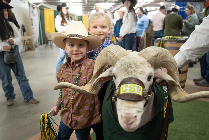 Two small kids taking a picture with Cam the Ram the animal at C S U Day at the Stock Show.