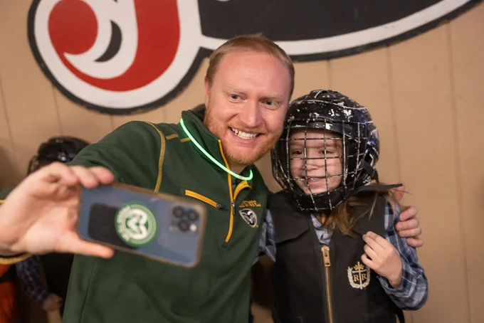 A parent wearing a C S U shirt taking a selfie with his kid before the kid goes mutton busting.