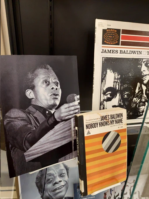 Black and white photos of James Baldwin speaking at BGSU, LP of Baldwin's The Struggle which has drawn profiles of him on the cover, and a rare copy of Baldwin's Nobody Knows My Name (from the CAC), which has yellow, orange, grey, and black and white stripes.
