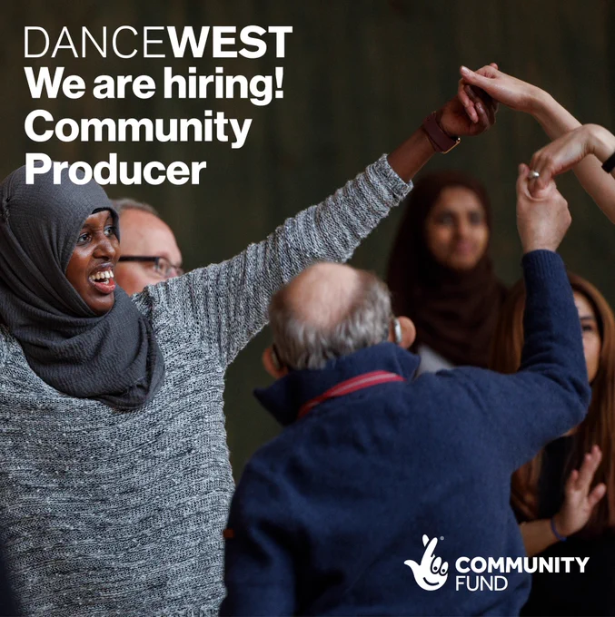 Three dancers from join hands. The dancer in the foreground is wearing a grey jumper and grey hijab, she smiles as she reaches towards the others hands. 