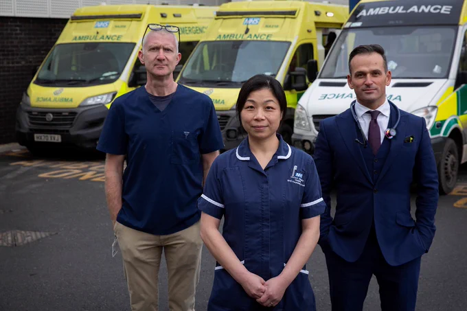Three people stand in front of three ambulances