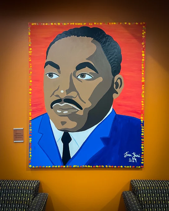 A painting of Dr. Martin Luther King Jr. —  wearing a blue suit and black tie, looking to the viewer’s left — hangs on an orange wall in the Student Union on the campus of UT Dallas.
