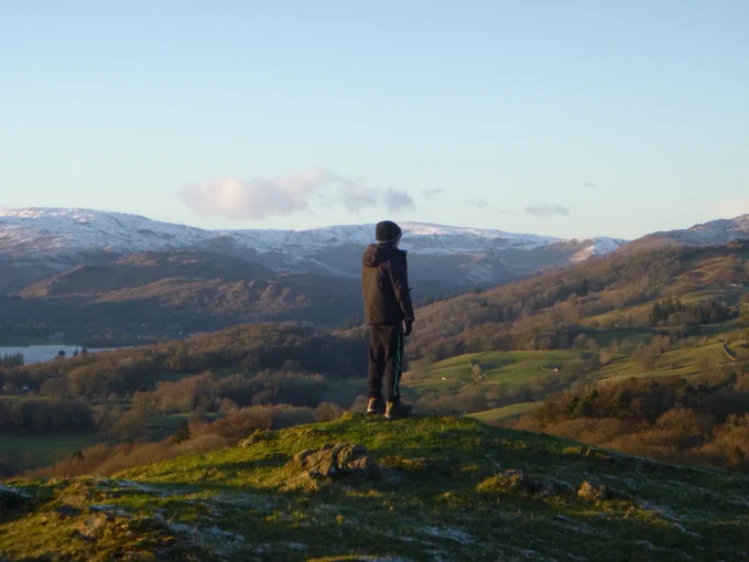Pupil on school trip stood on hill top looking at snow capped mountains