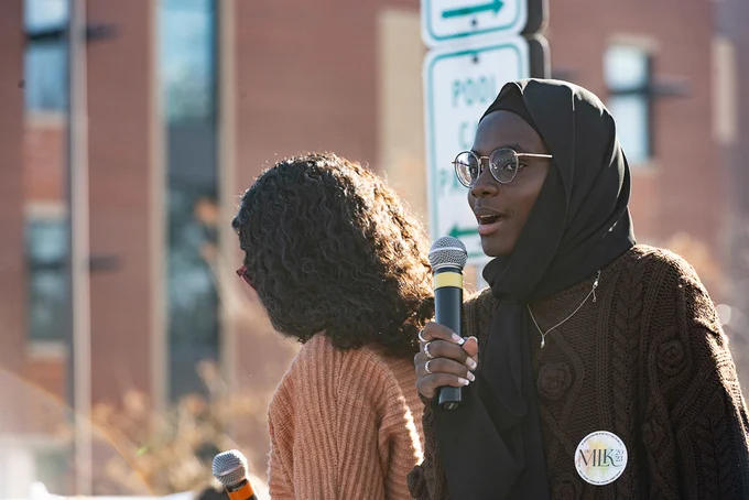 M L K Day March speaker addresses the crowd while holding a microphone. 