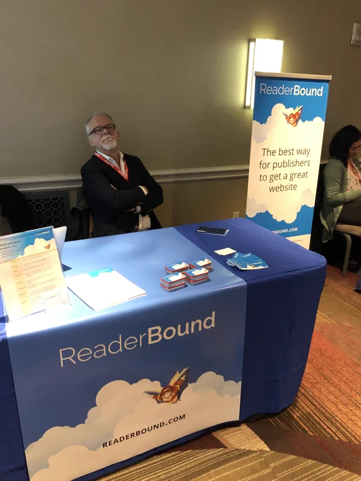 Doug from ReaderBound smiling at a table with material on the best way for publishers to get a great website