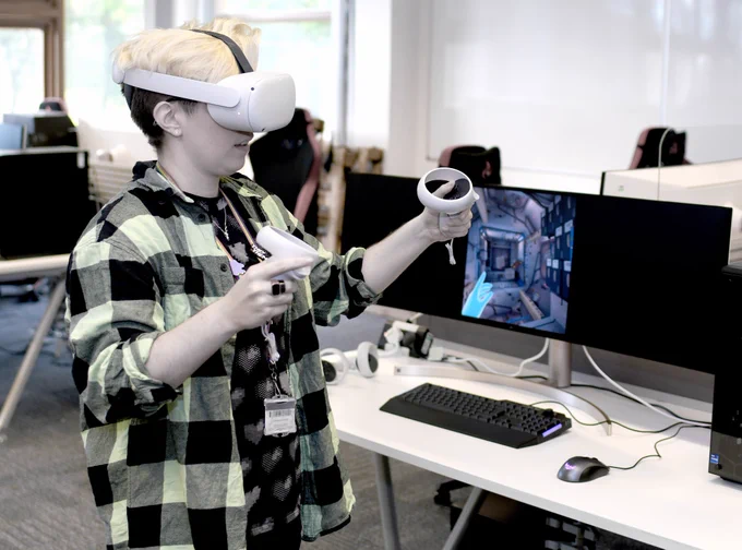 Person in a checked shirt using a virtual reality headset and controllers in the creativity lab