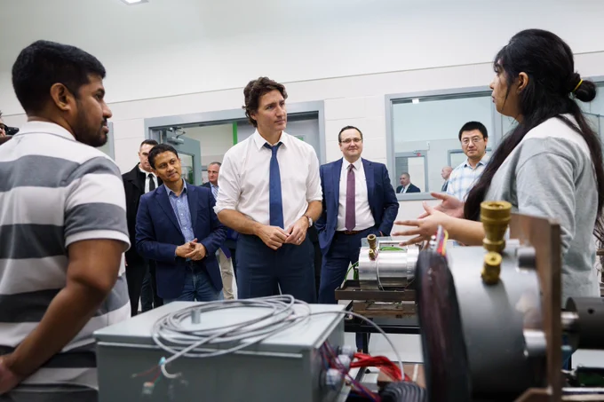 Prime Minister Justin Trudeau, Member of Parliament Irek Kusmierczyk, and Dr. Narayan Kar are standing indoors and speaking with University of Windsor students.