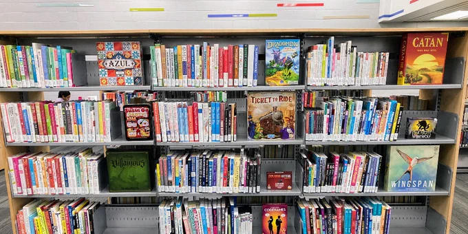 Book shelf with books intermixed with board games. 