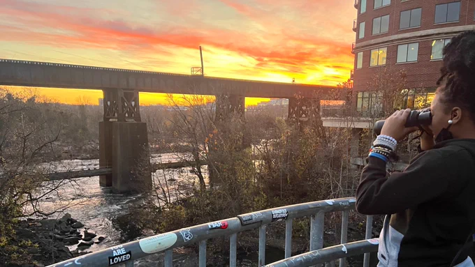 2 photos each show a student using binoculars to observe wildlife. In the background is a vibrant sunset, a bridge, & a building.