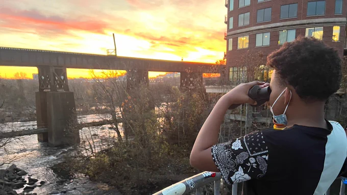2 photos each show a student using binoculars to observe wildlife. In the background is a vibrant sunset, a bridge, & a building.