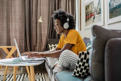 Person seated on a sofa in pajamas, wearing a headset and working on a laptop computer.