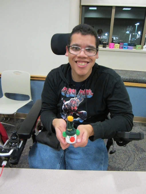 A person in a wheelchair shows off a snowman in a green hat with an orange pom
