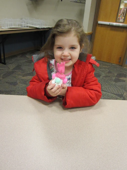 A kid shows off a snowman in a pink hat