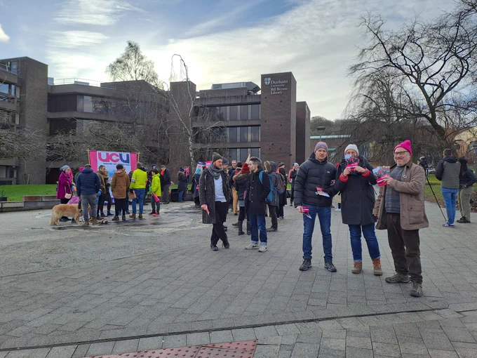 People standing on a picket line, many carrying placards and wearing pink UCU hats