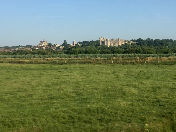 Green fieds in the foreground with castle and town visible in the background, taken from the train.