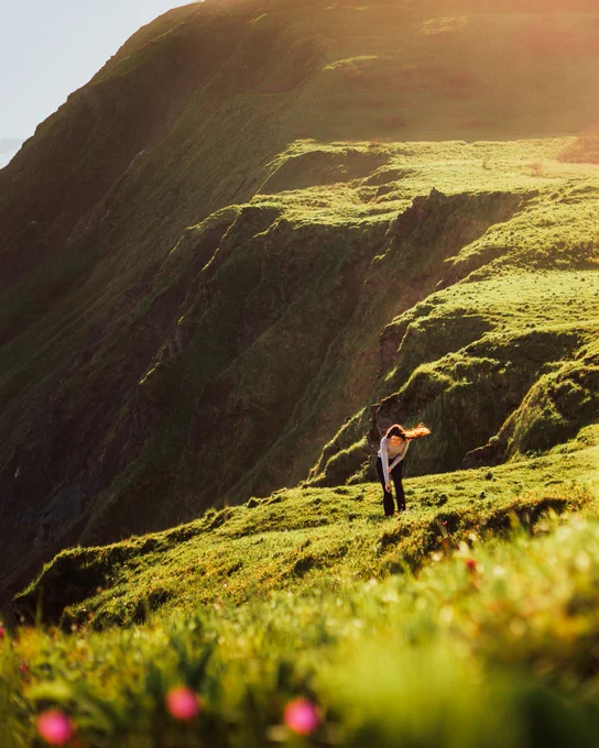 A photo of a woman picking flowers on a cliff on Kodiak Island. Photo taken by Alaskan photographer, Ellen Carty.